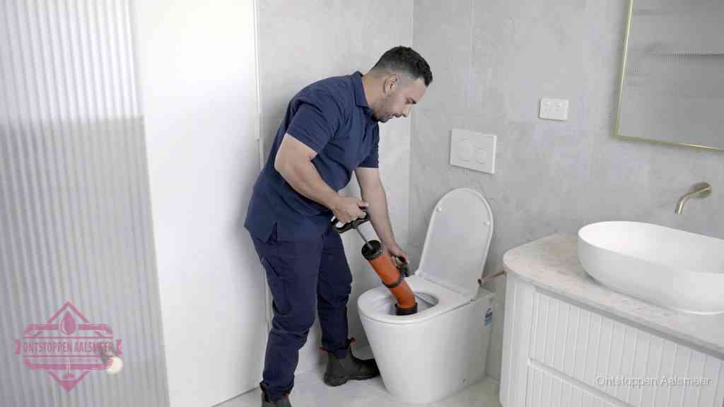 Een monteur buigt over een wandcloset en duwt met de hand een persluchtontstopper in de toiletpot om de verstopping handmatig los te maken in Aalsmeer