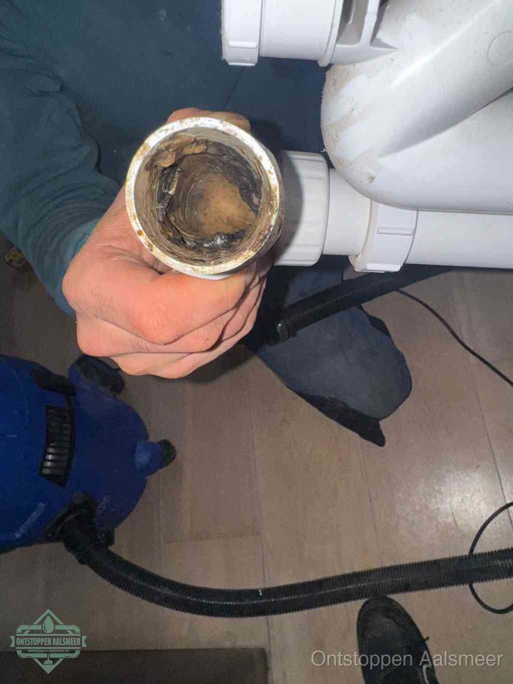 Een hand houdt een losgekoppeld PVC-afvoerbuisstuk vast dat van binnen volledig is dichtgeslibd met vet, vuil en aanslag, de meest voorkomende oorzaak van een verstopte afvoer in Aalsmeer