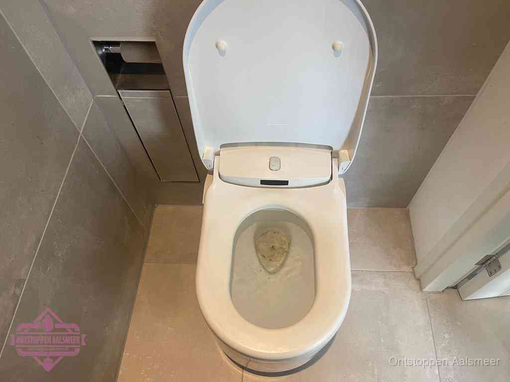 Een wit hangtoilet waarin een prop wc-papier op het water blijft drijven, een duidelijk signaal van een verstopte wc in Aalsmeer