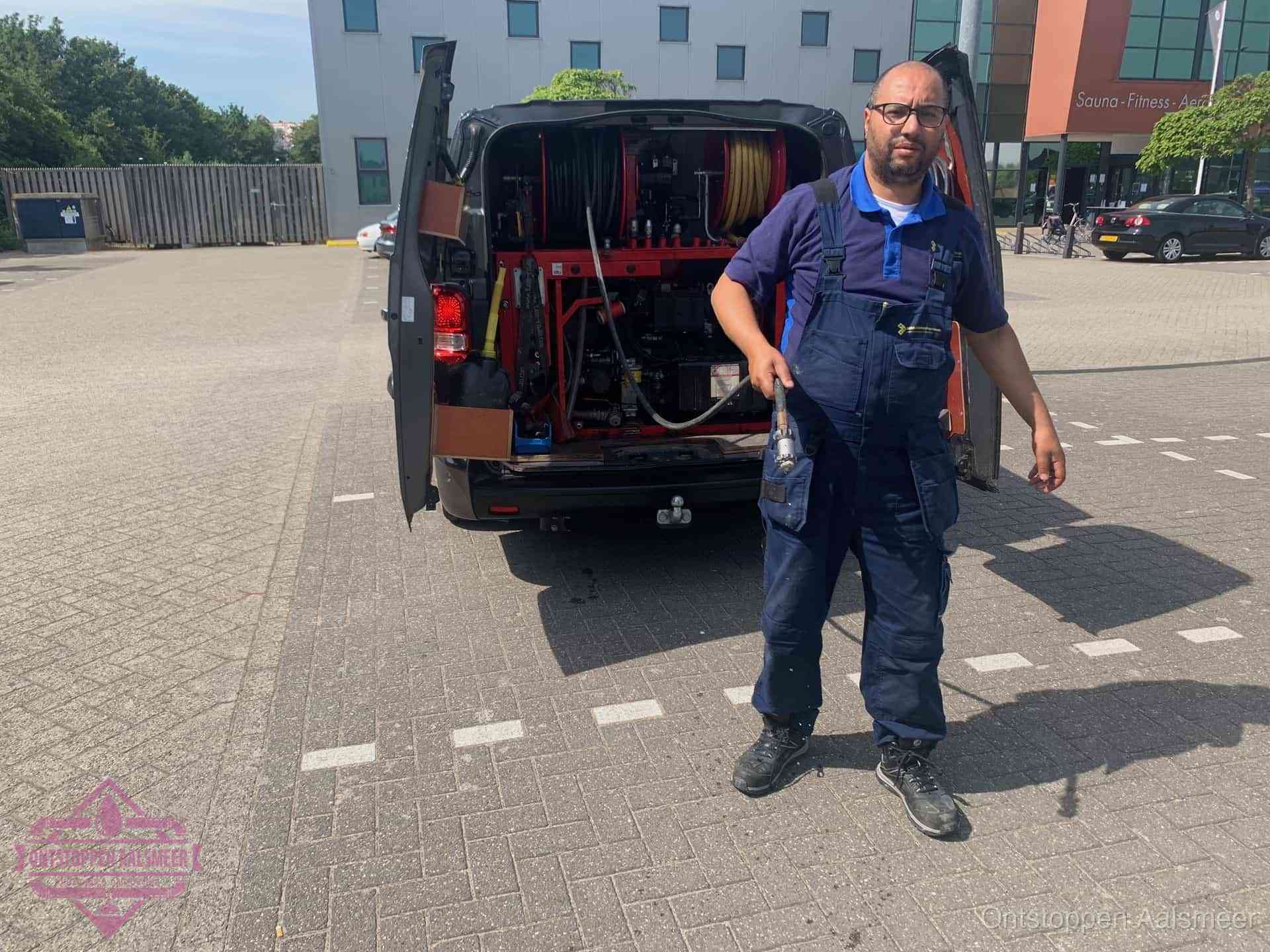 Een monteur bij zijn bestelbus met een hogedruk- en rioolreinigingsunit, klaar om de oorzaak van terugkerende wc-verstoppingen aan te pakken in Aalsmeer