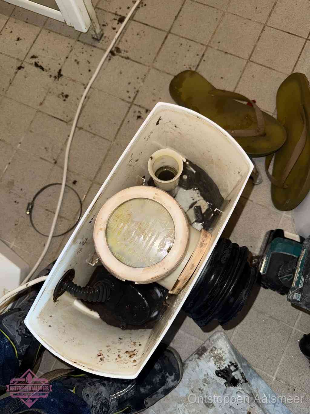 Een gedemonteerde toiletpot op de vloer met ontstoppingsveer en gereedschap ernaast, het verwijderen van een vastzittend voorwerp uit de wc in Aalsmeer