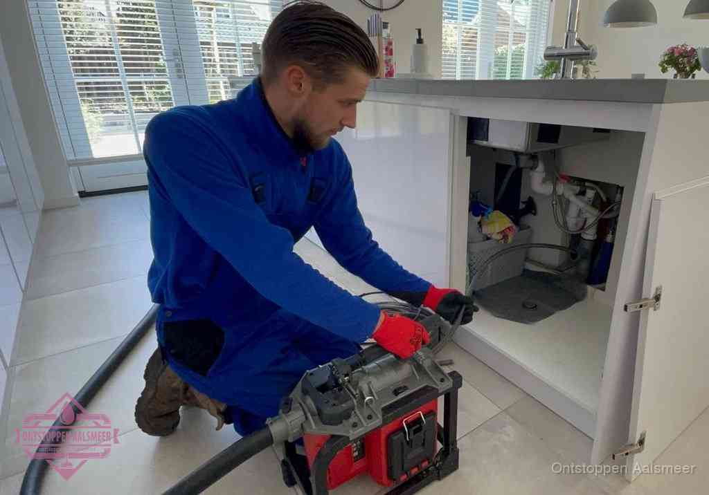 Een monteur voert een professionele elektrische ontstoppingsmachine in de afvoer onder de spoelbak tijdens het gootsteen ontstoppen in Aalsmeer