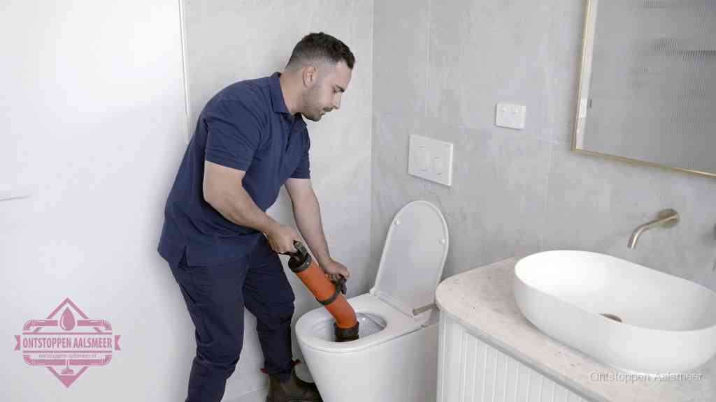 Een man gebruikt een handmatige luchtdruk-ontstopper in een modern betegeld toilet om zelf de wc te ontstoppen in Aalsmeer